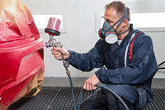 Man in a painting mask and protective clothing spray painting a piece of equipment