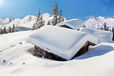 Color image of snowed-in cabins with mountains and pines in the background