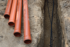 Four copper colored pipes setting next to a small dug-out trench with wires