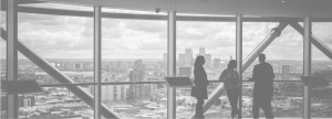 Black and white image of three people in a high rise building overlooking a city